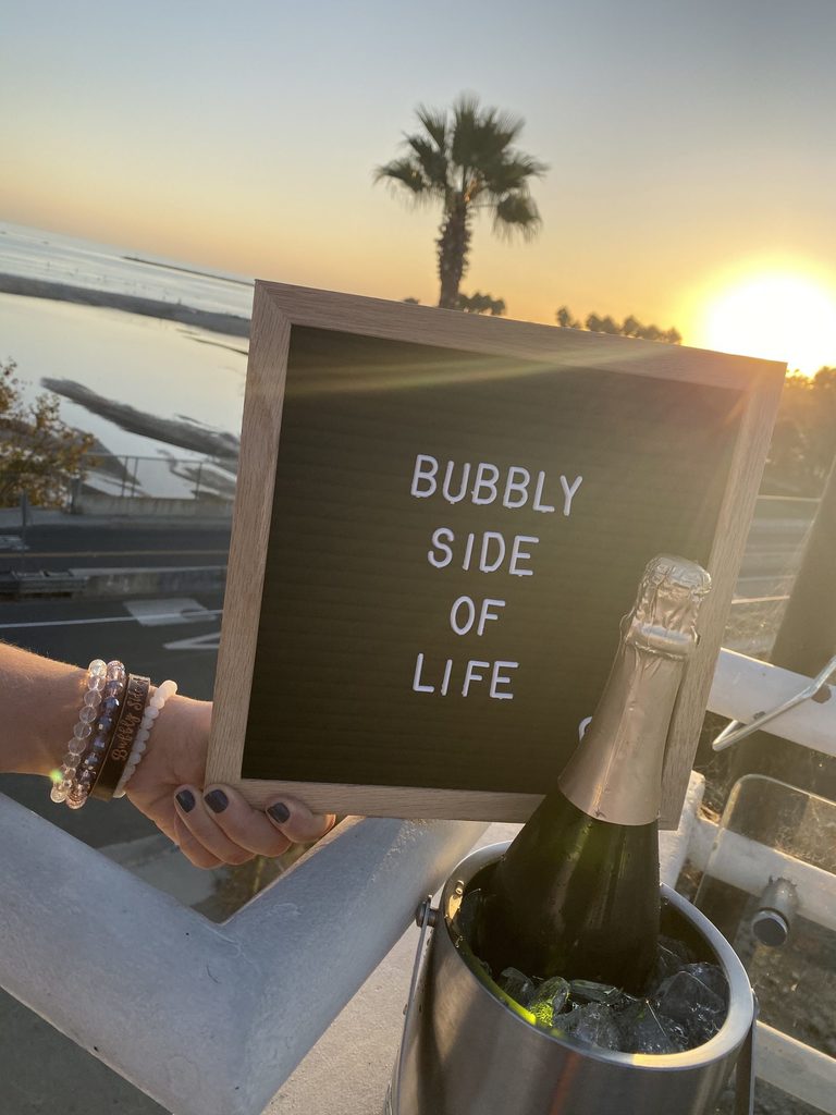 Letter board sign with Bubbly Side of Life in front of a beach view with champagne