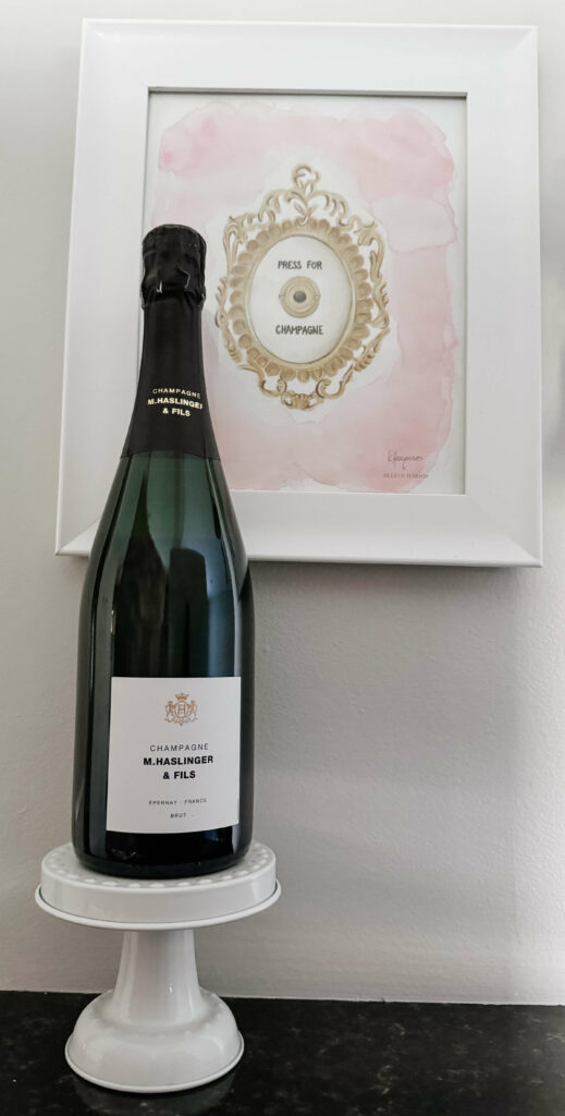 A bottle of Champagne M.Haslinger & Fils on a pedestal next to my favorite Press for Champagne print.