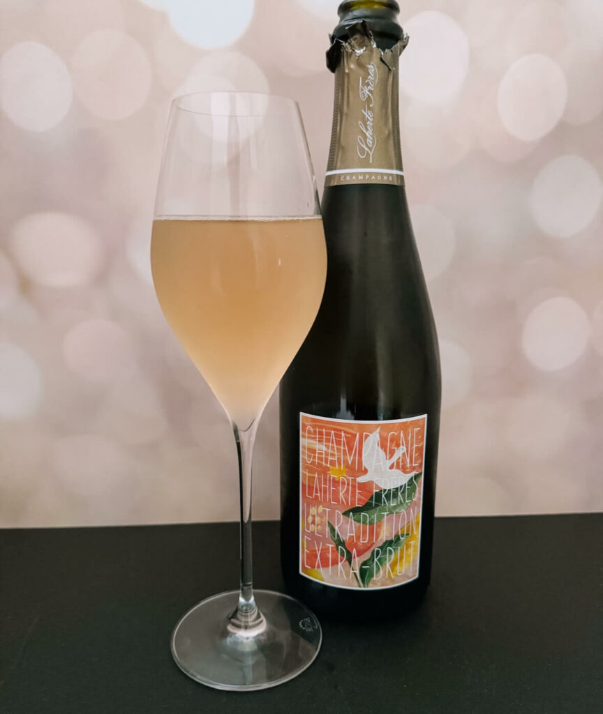 A bottle of Champagne Laherte Freres Ultratradition Extra Brut that I truly bought for the label showcasing the beautiful color in a tulip glass beside it.