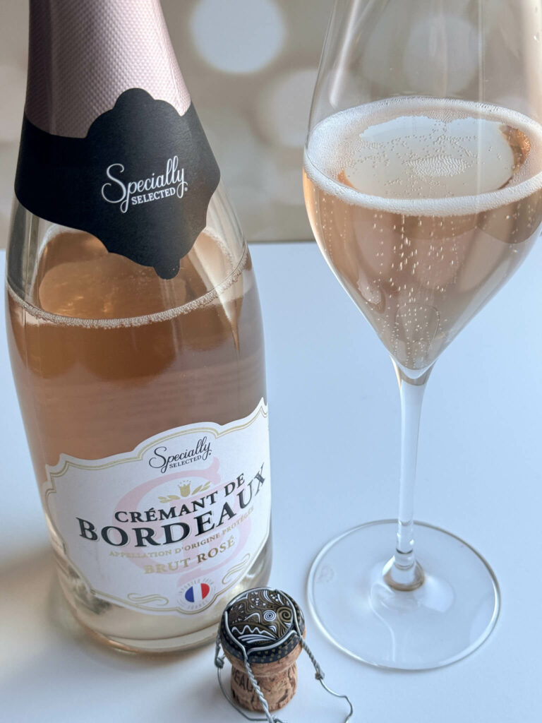 A bottle of Crémant de Bordeaux next to a champagne tulip half full with the sparkling rosé showing off the dancing bubbles in the glass.  
