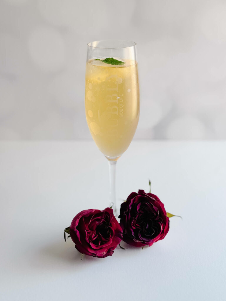 In a champagne glass surrounded by roses, is the official cocktail of the Kentucky Derby, a mint julep garnished with a mint sprig. 