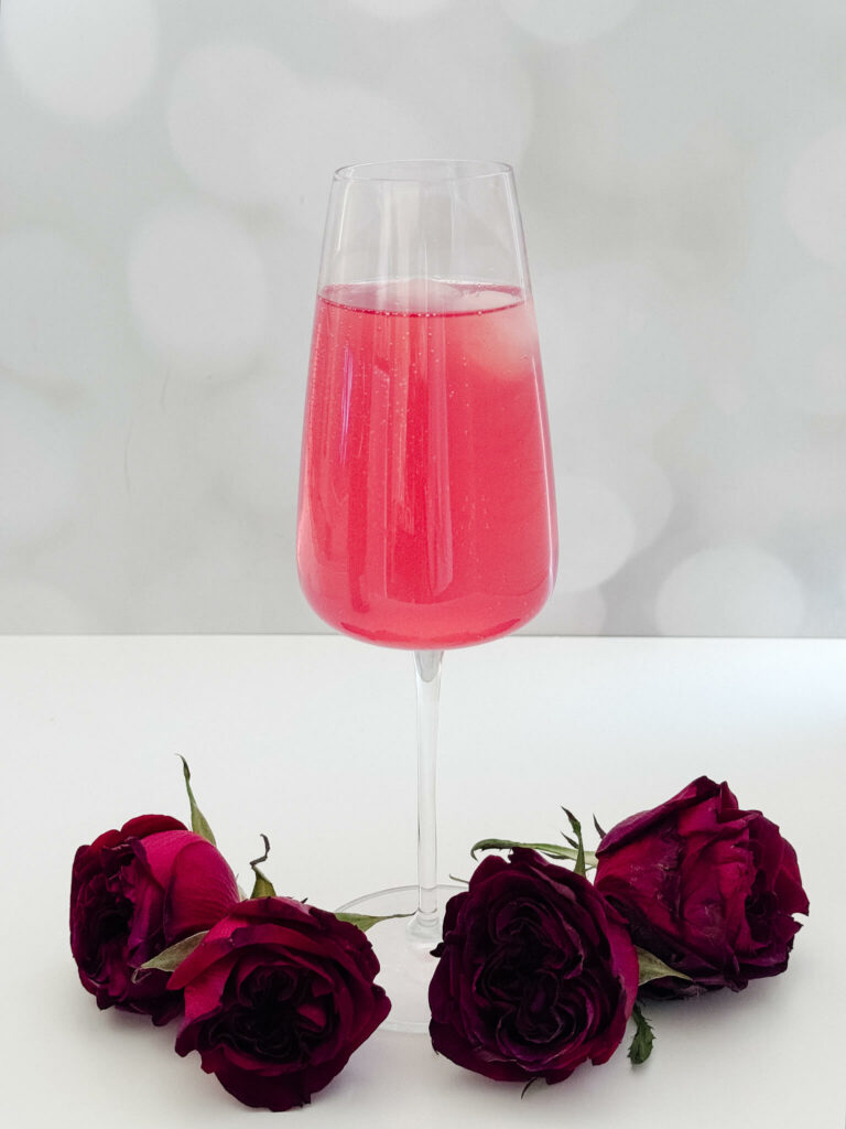 Another Kentucky Derby inspired cocktail called the Oaks Lily in a tall champagne glass surrounded by roses that we added sparkling wine to make it the perfect bubbly derby drink.